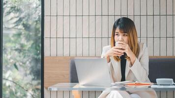 A contemplative businesswoman takes a coffee break at her laptop in a cafe, reflecting on her work amidst a serene setting. photo