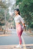 Fitness concept, Fit young female runner stretching her leg during a warm-up in a sunny park pathway. photo