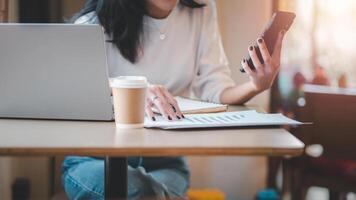 Business freelance concept, An entrepreneur is engaged in analyzing a data chart on her smartphone, alongside her laptop and coffee in a dynamic work environment. photo