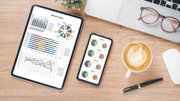 Business analytics concept, Tablet and smartphone displaying colorful charts and graphs on a wooden desk with a laptop, glasses, and a cup of coffee. photo