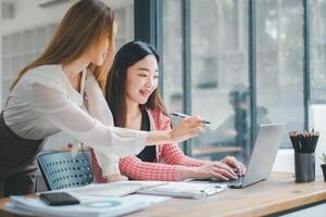 Business team analytics concept, Two engaged colleagues collaborating on a project with a laptop at a wooden desk in a bright, modern office space. photo