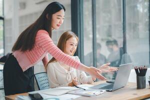 Business team analytics concept, Two female colleagues engaging in a productive discussion over a laptop in a well-lit, modern office environment. photo