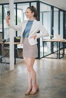 Business relax concept, Joyful businesswoman in smart casual attire taking a selfie with her smartphone in a spacious and modern office. photo