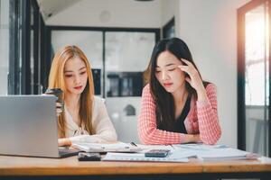 Business team analysis concept, Two focused colleagues analyzing data on a laptop in a well-lit work environment, one holding a coffee cup. photo