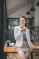 Smiling young professional woman taking a coffee break in a modern office setting, exhibiting confidence and relaxation. photo