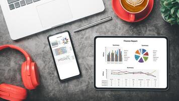 A high-tech professional workspace featuring a tablet displaying colorful financial graphs, paired with a laptop, headphones, and a cup of coffee. photo