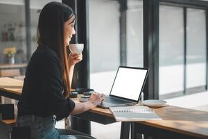 A young professional female takes a relaxing coffee break at a modern workspace, with a laptop and notebook on her wooden desk. photo