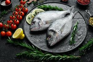 Fresh Dorado fish with spices is ready to cook. On a plate. On a black stone background. photo