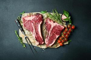 Dry-aged Raw T-bone or porterhouse beef steak with herbs and salt. On a black stone background. Barbecue. photo