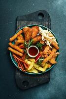 Fast food. Plate with snacks nuggets, sausages, French fries, cheese sticks. On a black stone background. Free space for text. photo