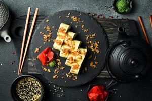 Japanese sushi with fish and cheese on a rustic dark background. Sushi rolls, nigiri, maki, pickled ginger, wasabi, soy sauce. Sushi set on a table. photo