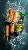 Fresh crispy baguette, a jar of oil and a rolling pin on a dark background. Free space for text. photo