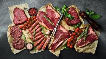 A set of juicy raw steaks, kebabs, cutlets and meat with spices and herbs. On a black stone background. Top view. photo