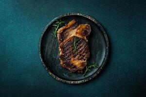 Grilled ribeye beef steak with spices on a wooden plate. On a dark blue stone background. Top view. photo