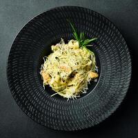 Pasta with pesto sauce and chicken in a black bowl. On a dark background, close-up. photo