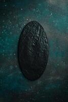 Oval slate black plate. On a dark green-turquoise background. Free space for text. photo