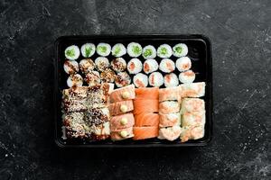 Sushi y rollos chino comida colocar. sacar, comida entrega. en un negro Roca antecedentes. foto