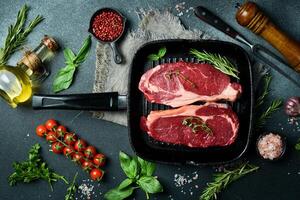 Juicy rib eye beef steak with spices and herbs on a pan. Ready to cook. On a dark stone background. photo