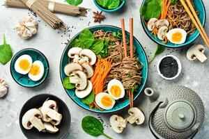 Japanese soba noodles with egg, mushrooms and microgreens. On a gray stone background. Top view. photo