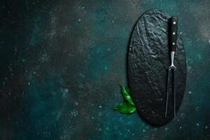 Slate plate and Metal fork for meat and steaks. On a dark green-turquoise background. Free space for text. photo