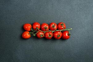 Fresh red cherry tomatoes on a branch. Vegetables. On a black stone background. Top view. photo