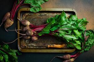 Raw organic beetroot and beetroot leaves, on a dark background, close-up, top view. photo