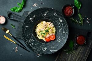 Carbonara pasta with bacon and cheese. In a black plate. Italian cuisine. On a dark background, close-up. photo