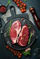 Two raw rib eye beef steaks with spices on a plate. Ready to cook. On a dark stone background. Top view. photo