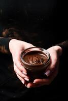 Female hands hold a glass jar with melted chocolate. Kitchen utensils. On a black background. photo