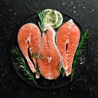 Raw juicy salmon steaks are ready for cooking. On a dark table. Top view. photo