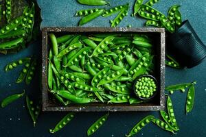 Pods of green peas with leaves in a wooden box. On a black stone background. Top view. Healthy food. photo