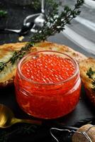 Jar with red natural caviar. Macro photo. Caviar. On a black background. photo