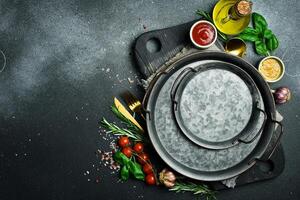Kitchen banner. A kitchen table on which vegetables, spices and a metal tray are laid out. On a dark stone background. free space for text. photo