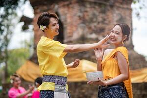 un hermosa joven tailandés Pareja vistiendo tailandés disfraces jugando en el agua durante Songkran en el templo foto