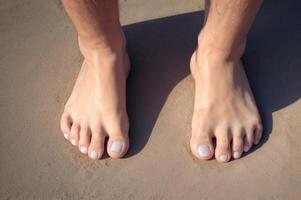 AI generated A pair of feet with white nail polish stand on sand. ai generative photo