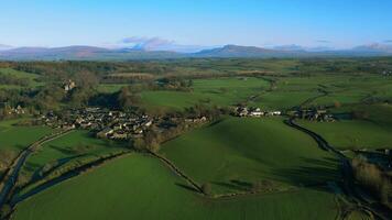 Aerial view of a lush countryside with a small village, green fields, and distant mountains under a clear sky. video