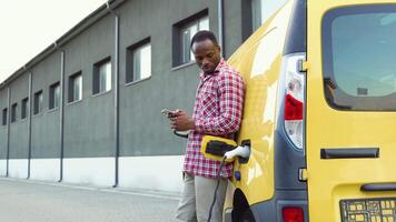 Preto homem segurando Smartphone enquanto cobrando caminhão carro às elétrico veículo cobrando estação video