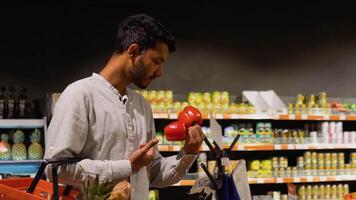 lado Visão do indiano homem comprando tomate e Pimenta. ásia homem segurando compras cestas e escolhendo fresco legumes dentro supermercado video