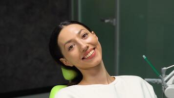 giovane sorridente donna seduta su sedia a dentista ufficio. dentale cura, salutare denti video