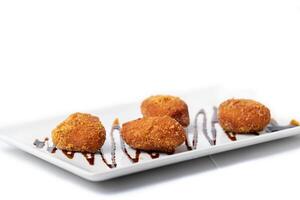 assortment of croquettes with a vinaigrette on a white rectangular plate photo