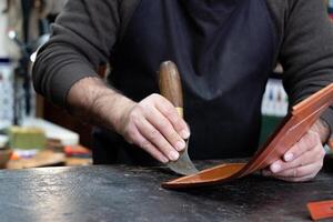 hands of craftsman working the leather with special tool in a workshop photo