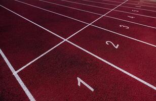 perspectiva ver de un rojo corriendo pista con blanco carril números y marcas, Listo para un carrera foto