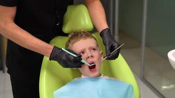 verdrietig bang weinig jongen opening zijn mond breed gedurende behandelen tanden door de tandarts. kind is bang naar traktatie tanden video
