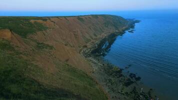 Aerial view of a rugged coastline with steep cliffs descending into a serene blue sea at dusk. video