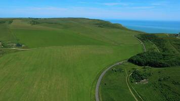 aérien vue de une enroulement route par luxuriant vert collines avec une clair bleu ciel et océan dans le Contexte. video