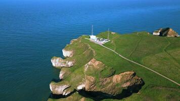 Antenne Aussicht von ein Leuchtturm auf ein Grün Küsten Cliff mit das Ozean im das Hintergrund. video