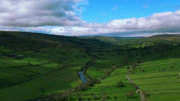 Aerial view of a lush green valley with meandering river, patchwork fields, and rolling hills under a cloudy sky. video