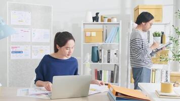 deux Jeune asiatique Commencez entreprise les partenaires concentrer et pense dans une décontractée petit affaires bureau, travail emplois avec tablette et ordinateur portable, comme en ligne free-lance commerce électronique entrepreneurs et collaborateur équipe. video