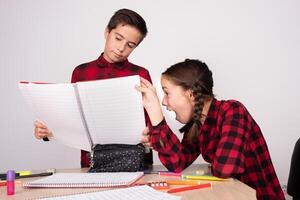 surprised girl looking at open notebook of indifferent child at school photo