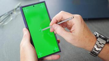 Close up view of man hand holding smart phone with green chroma key screen and stylus pen at his creative workspace. High quality 4k footage video